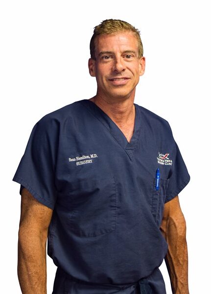Dr. Sean Hamilton in surgical scrubs smiling.