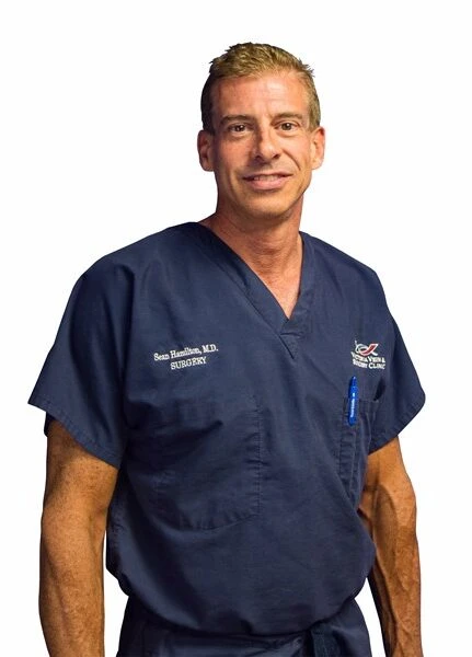 Dr. Sean Hamilton in surgical scrubs smiling.
